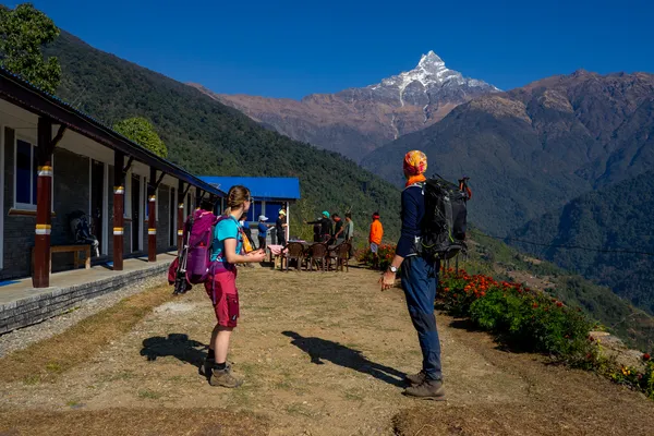 Trekkers outside a mountain lodge with wooded slopes and Machhapuchhre beyond