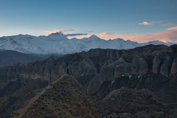 Golden light touching snow-covered mountains behind jagged rock formations of the high desert