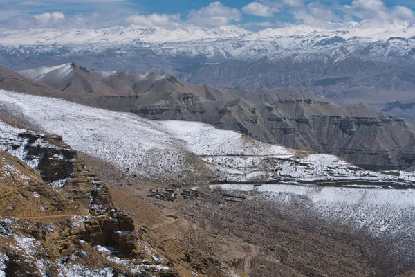 A cluster of traditional stone buildings nestled in a valley beneath snow-dusted hills