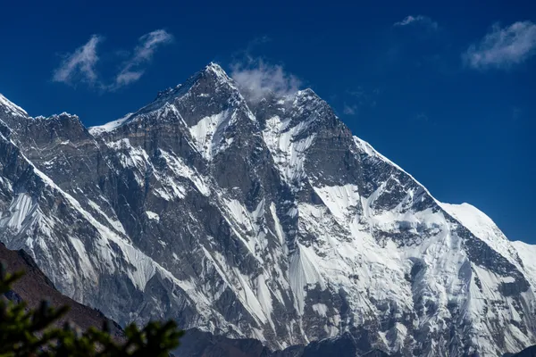 The sharp snow-covered summit of Thamserku towering over white clouds
