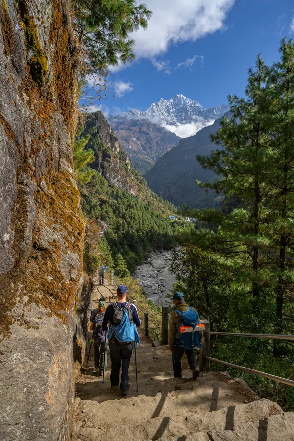 Trekkers descending stone steps with snow-capped Thamserku in the distance