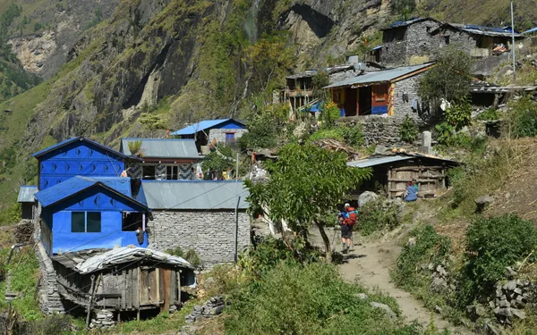 A hiker passing stone houses with bright blue roofs in the village of Thangurmu