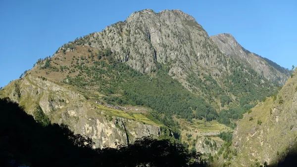 A massive grey rock face above green forest and terraced fields