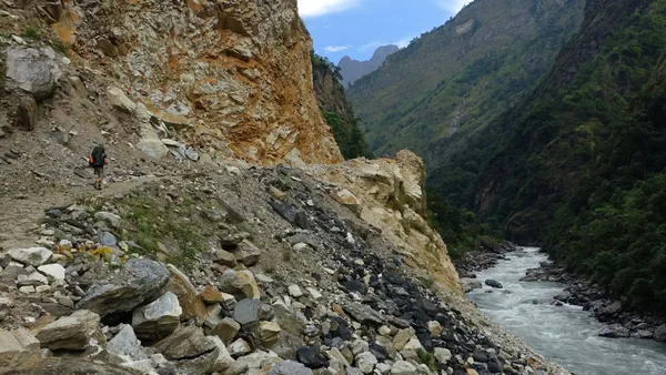 A trekker on a rocky path high above a rushing river