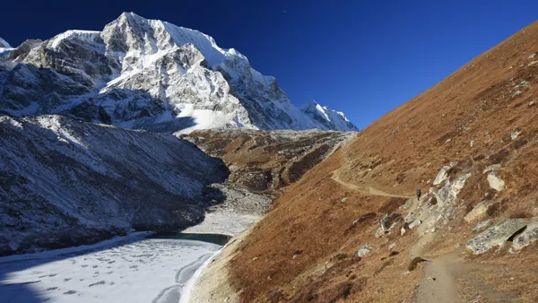 A narrow trail winding upward toward the snow-covered heights of Larkya La