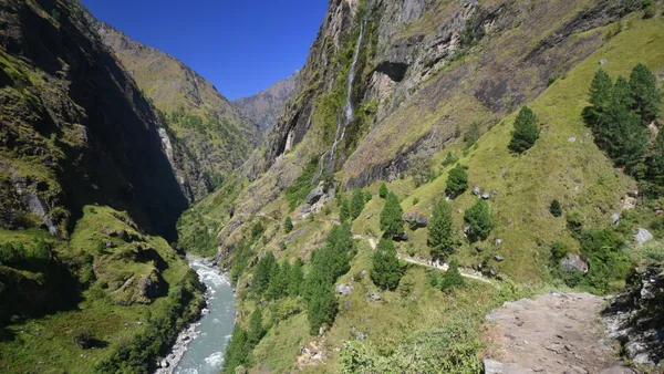 A tall waterfall plunging toward the river as the trail hugs the cliffside