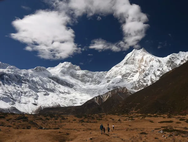 Hikers crossing the wide glacial moraine under the massive ice ridges of the Manaslu massif