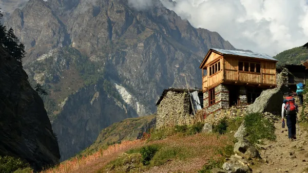 A hiker following a wildflower-lined path toward Rana with massive peaks rising behind