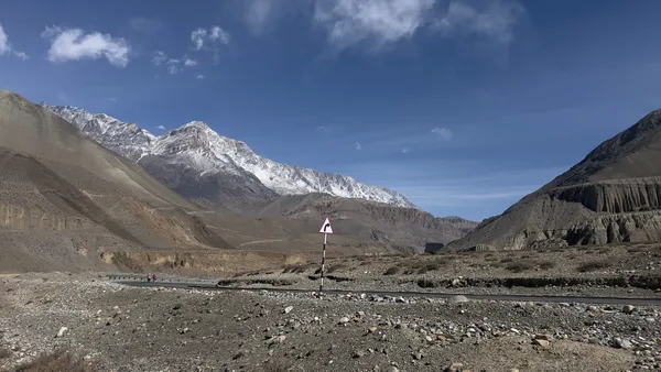A paved road snaking through arid rocky landscape toward snow-capped Himalayan peaks