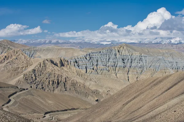 A high-altitude desert road winding above Ghami at 3,520 m toward distant snow-capped peaks